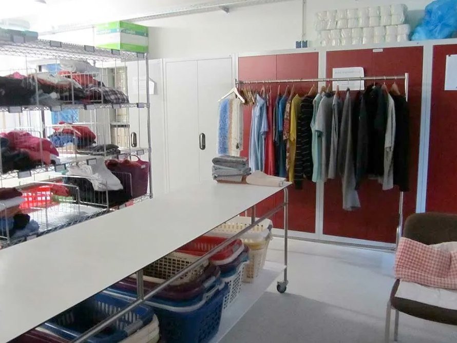 Raum mit Regalen und Wäscheständer, auf denen verschiedene Kleidungsstücke hängen oder eingeordnet sind