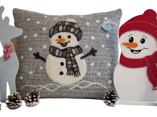 Eine weihnachtliche Dekorationssammlung mit zwei Rentier-Figuren aus Holz, einem grauen Strickkissen mit einem applizierten Schneemann und zwei Holzschnitten von Schneemännern in roten Mützen und Schals.