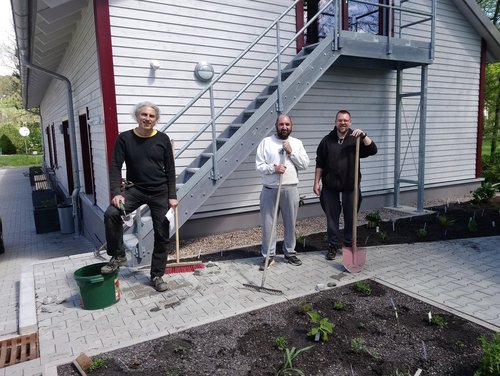 Drei Männer mit Gartengerät sehen vor dem Gemüsebeet stehend in die Kamera