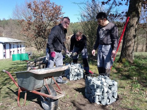 Drei Männer befüllen die zweite Gitterbox mit Steinen