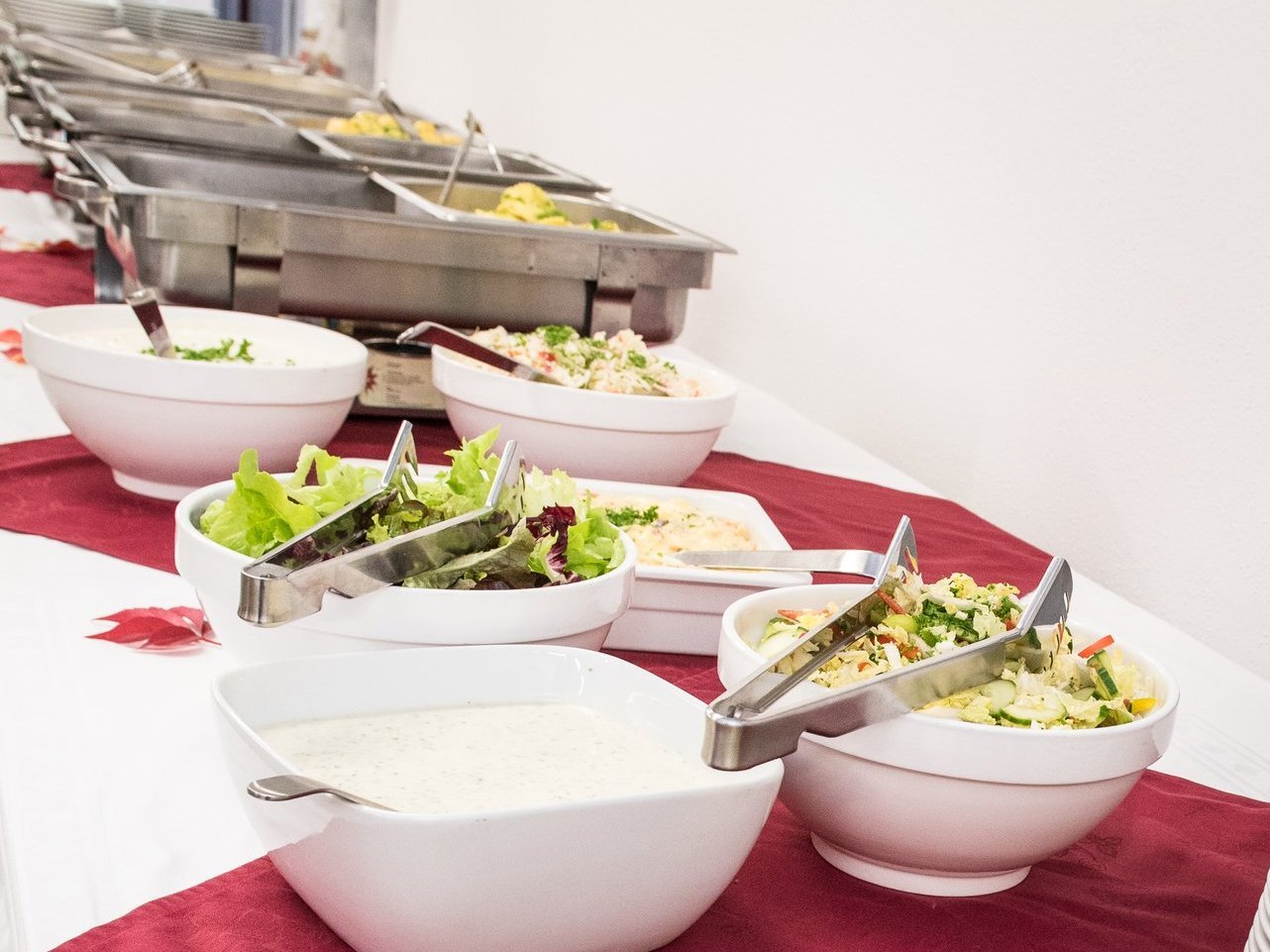 Essen am Buffet - es zeigt einen langen Tisch mit großer gemischter Obstschale, vielen Salaten mit Dressings und im Hintergrund sind verschiedene Hauptgerichte zu erahnen