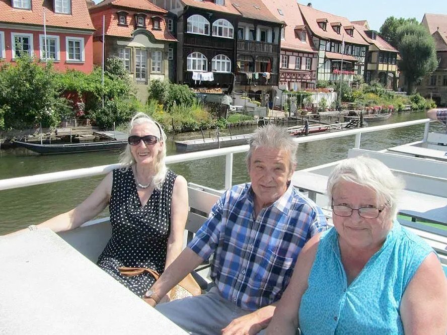 Flussfahrt auf einem Ausflugsboot: zwei ältere Fareuen und ein älterer Mann genießen den sonnigen Tag und lächeln in die Kamera