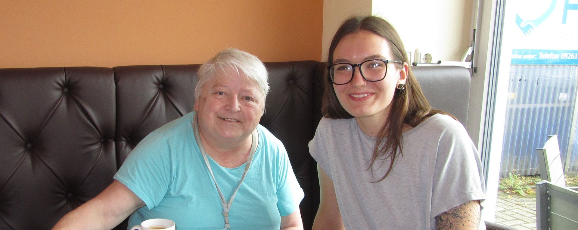 eine junge Pflegerin und eine ältere Frau bei Kaffee und Kuchen 